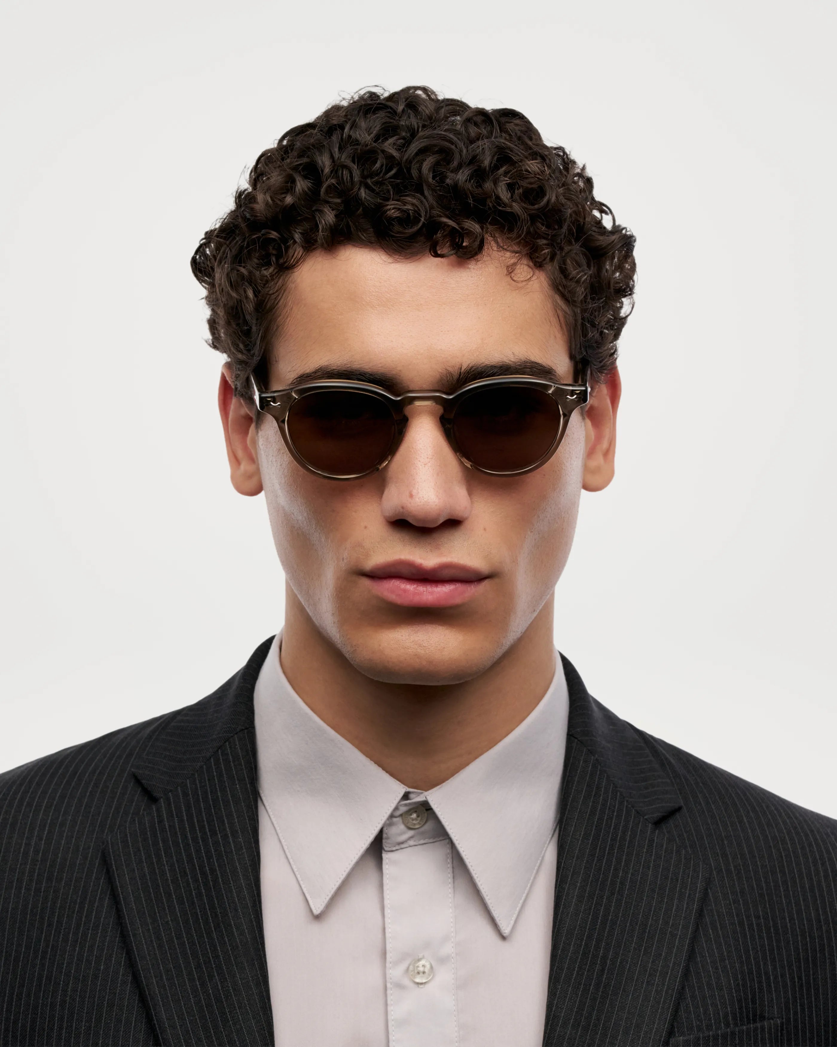 Scope Light Taupe Sunglasses worn by a model in a suit with curly hair against a neutral background.