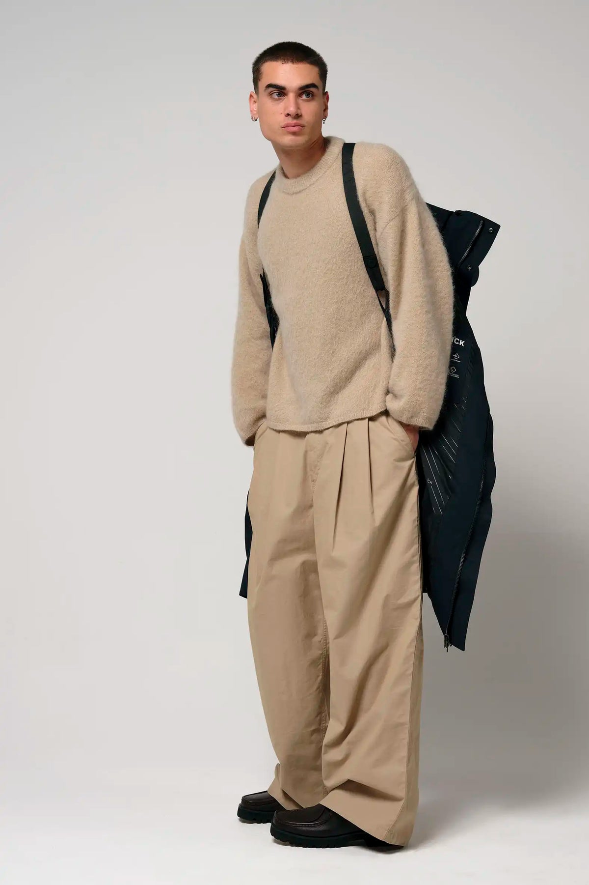 Model wearing beige sweater and oversized beige trousers, featuring a stylish black backpack.