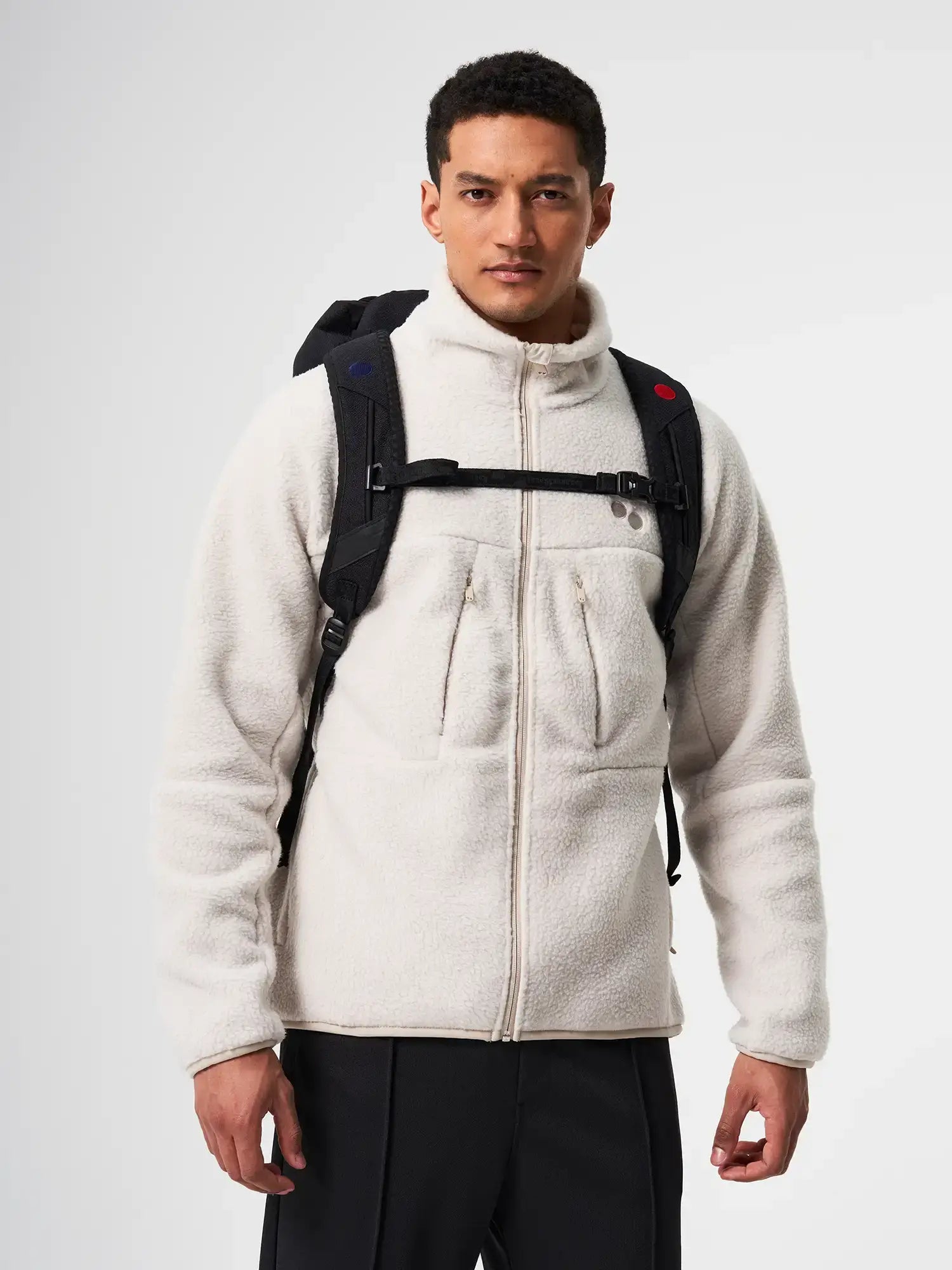 Model wearing a fleece jacket and carrying a Blok Large Licorice Black Backpack, showcasing modern outdoor style.