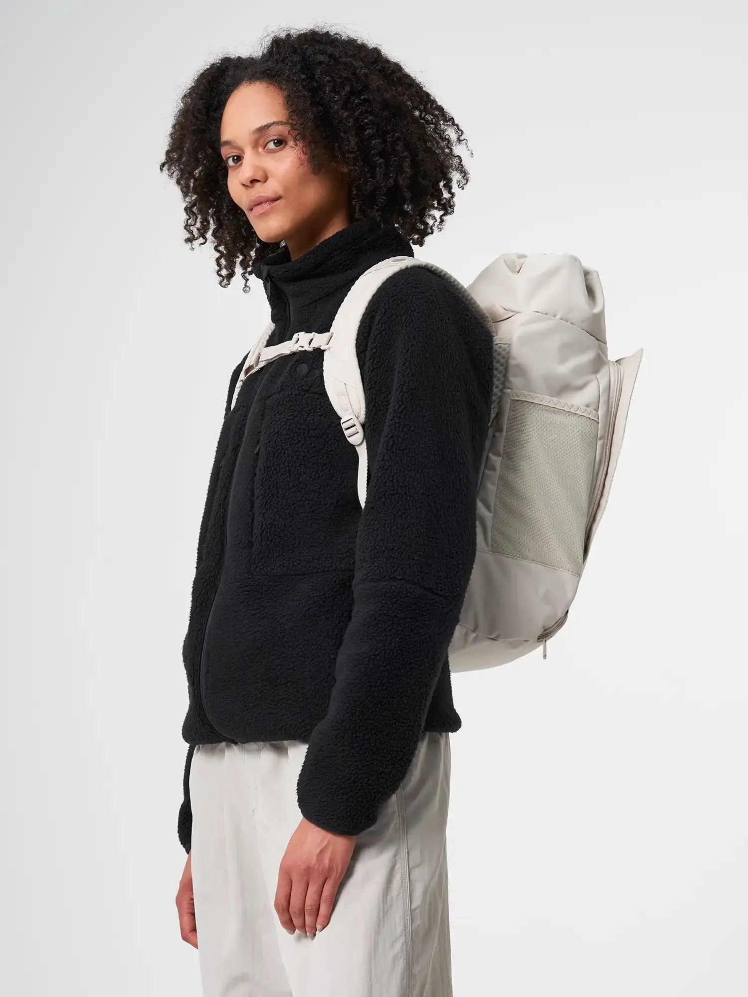 Model wearing Blok Medium Cliff Beige Backpack with black fleece jacket.