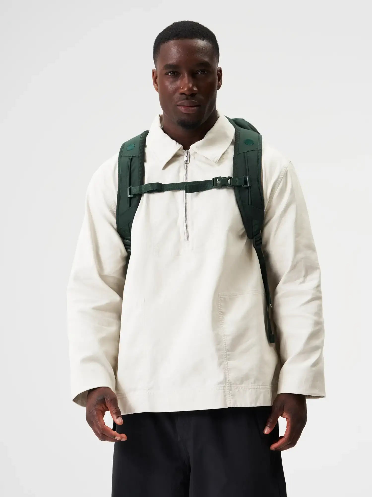 Man wearing a cream-colored jacket and Blok Medium Cosmo Green Backpack, showcasing a stylish outdoor look.