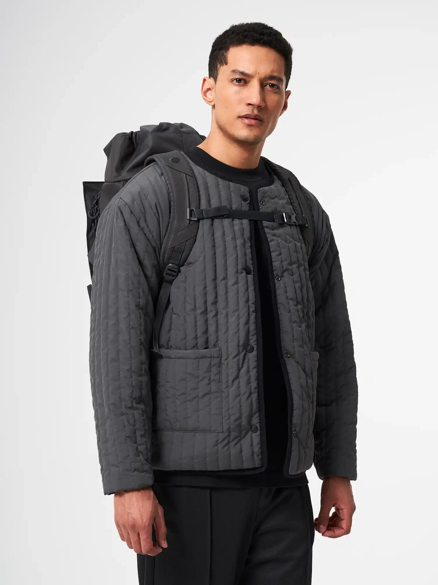 Man wearing a quilted gray jacket with a Blok Medium Deep Anthra Backpack on his back.