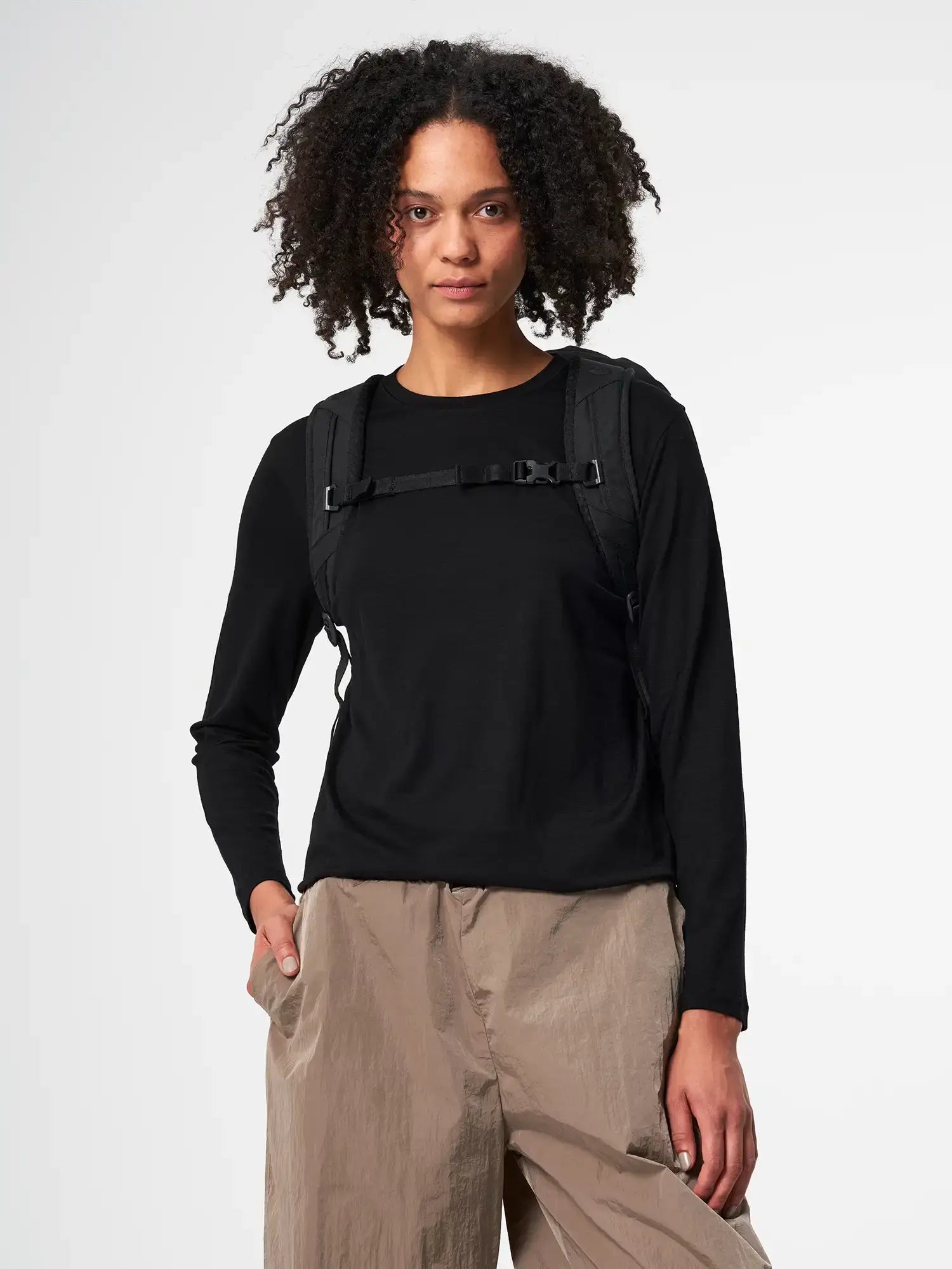 A model wearing a black top with the Blok Medium Rooted Black Backpack, showcasing its adjustable chest strap.