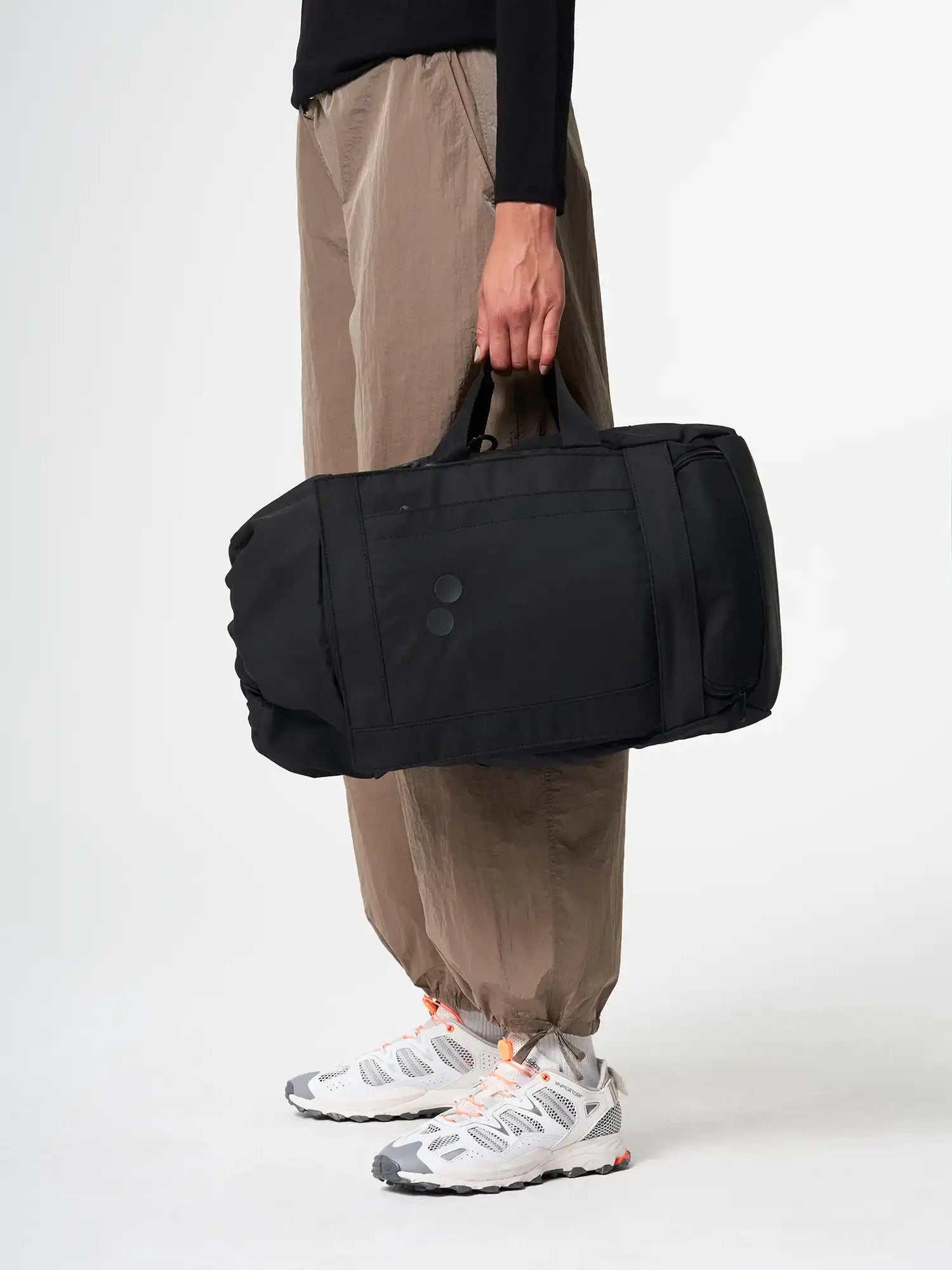 Blok Medium Rooted Black Backpack held by a model, featuring a sleek design and durable water repellent material.