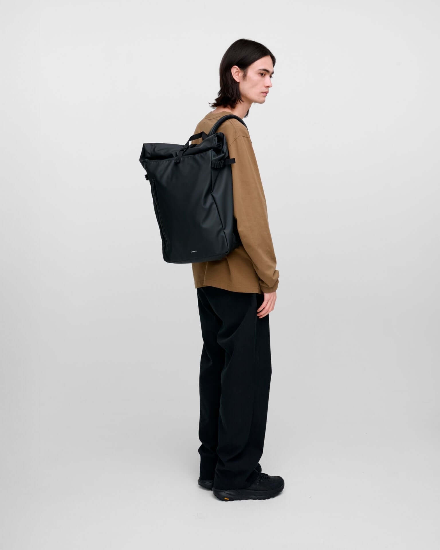 Person wearing Stream Slim Rolltop L Black Backpack in a stylish pose with a neutral background.