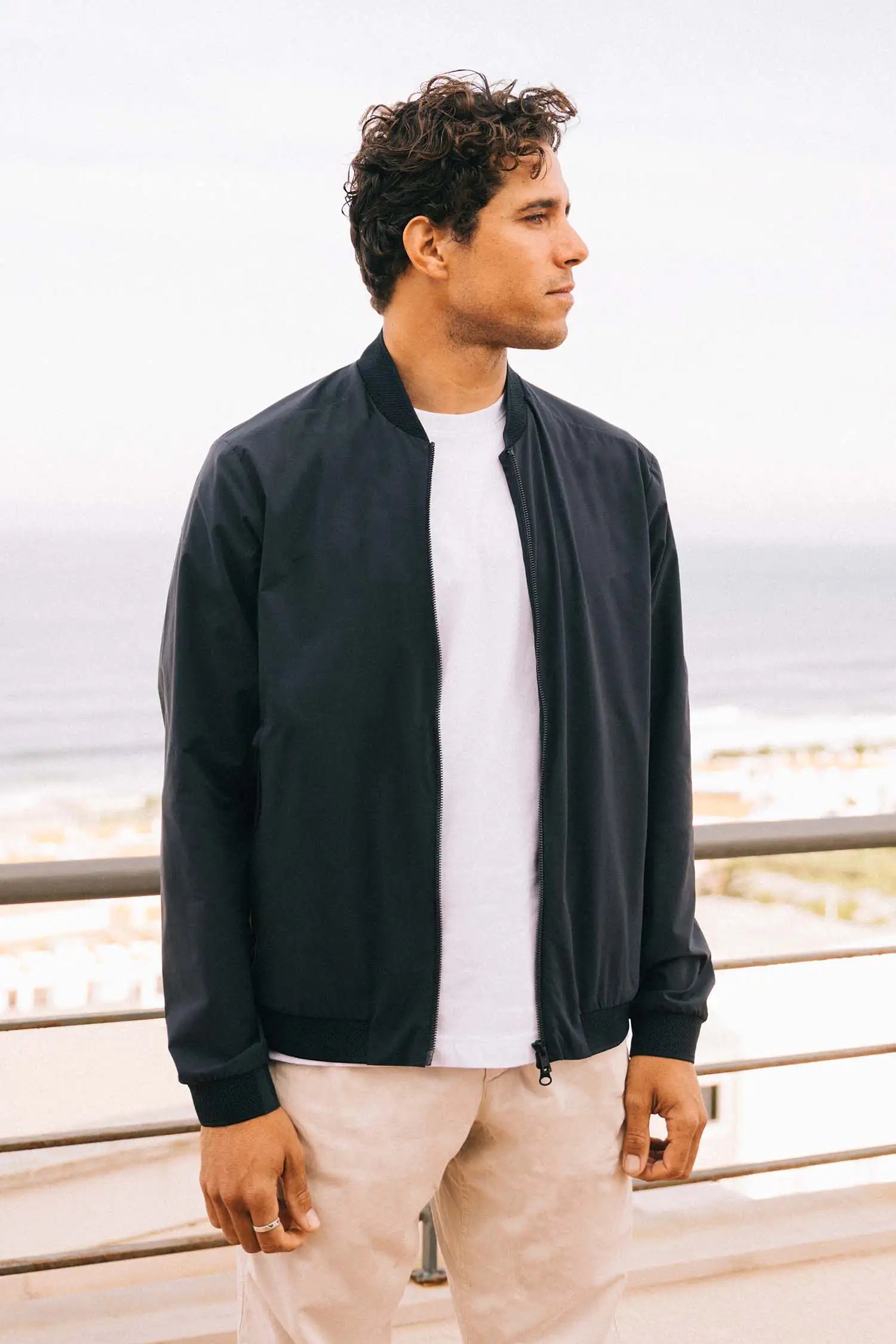 Campo II Navy Jacket model showcasing lightweight, windproof, and water-resistant features by the ocean.