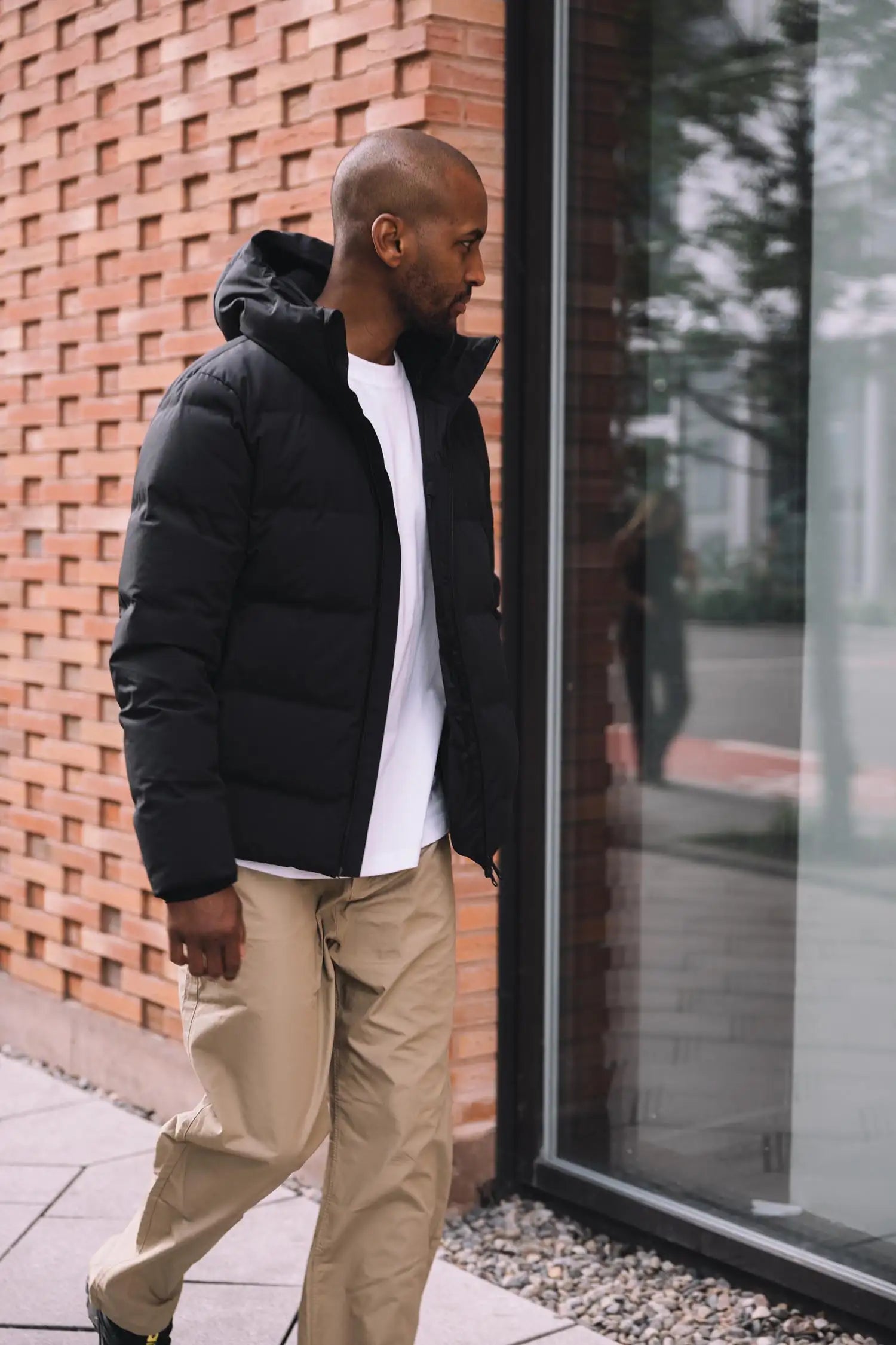 Man wearing Torrent II Onyx Coat walking by a modern building in a stylish urban setting.
