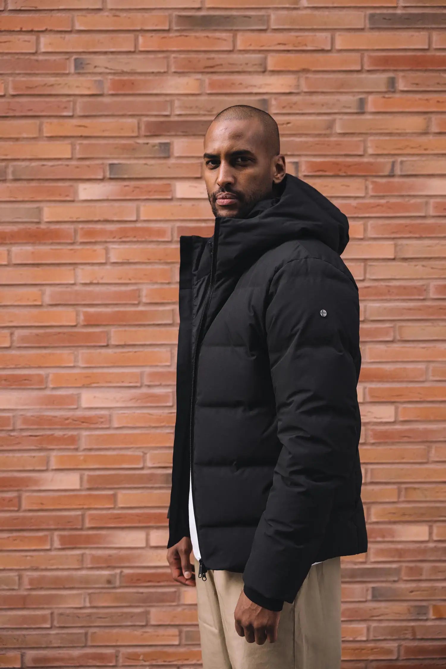 Model wearing the Torrent II Onyx Coat, showcasing its sleek design against a brick wall.