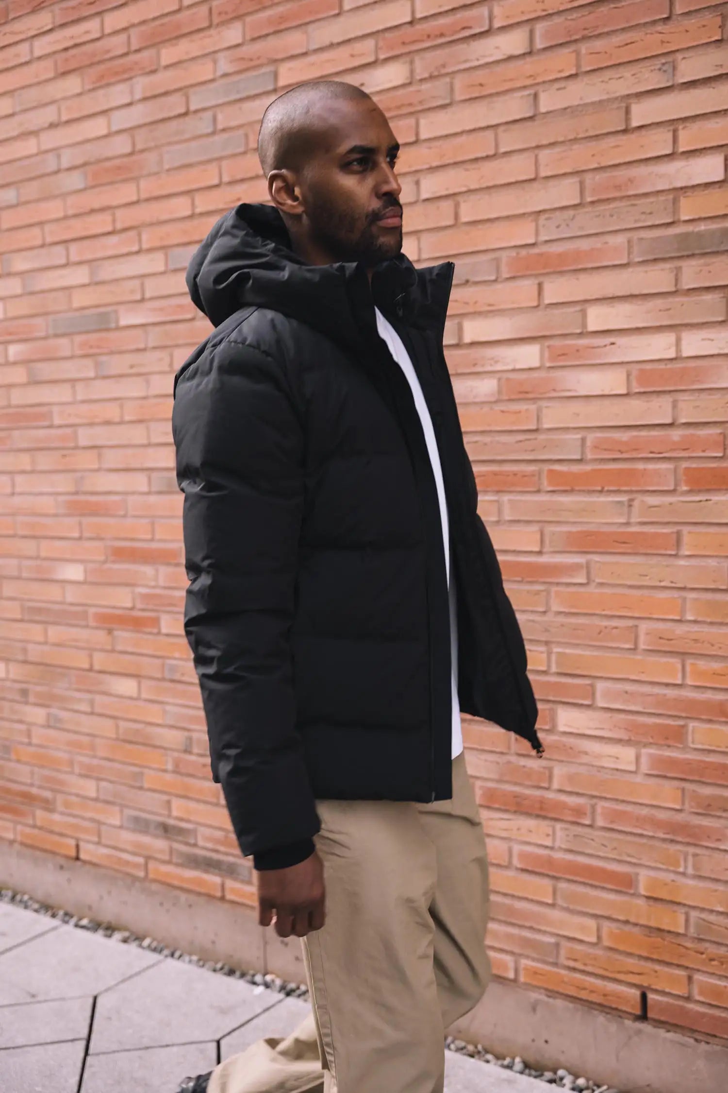 Man wearing the Torrent II Onyx Coat, showcasing its stylish and functional design against a brick wall.