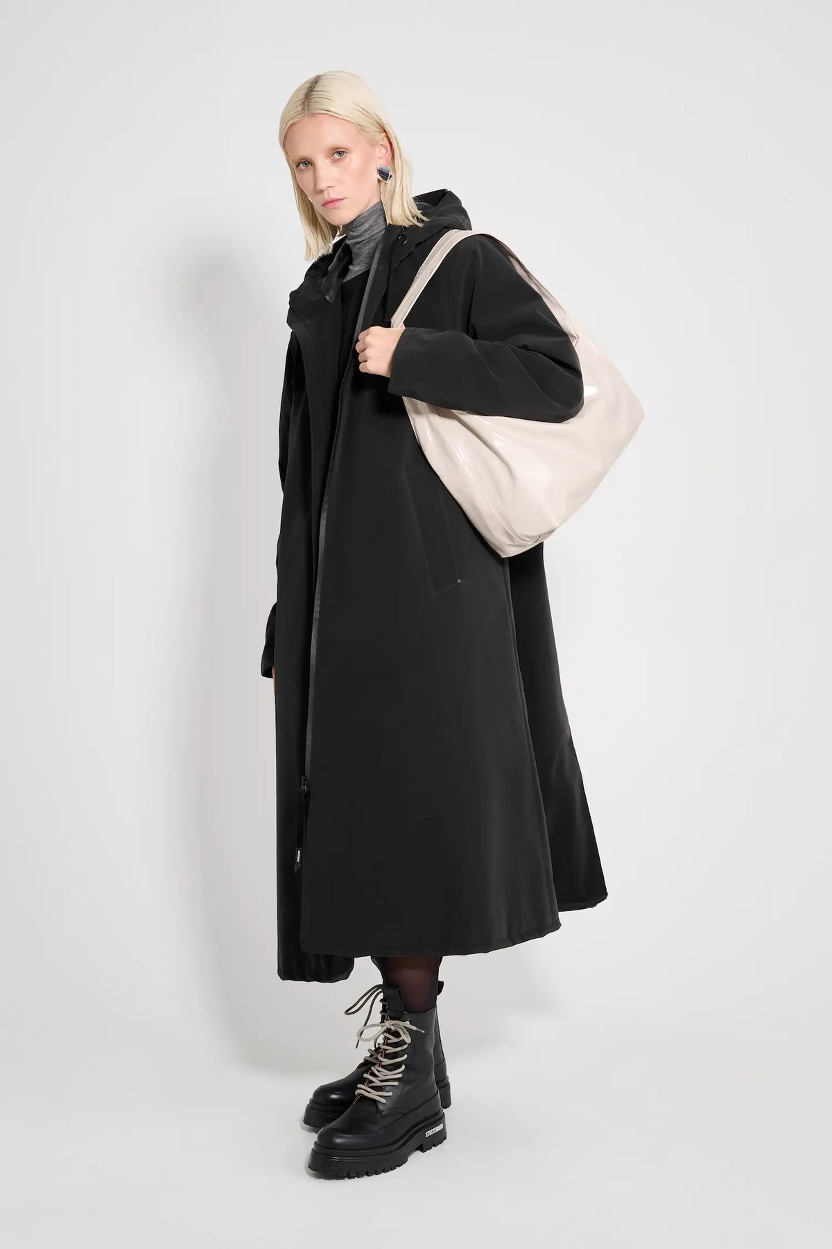 Mosebacke Long Matte Black Winter Coat worn by model with a beige bag and stylish boots on a white background.