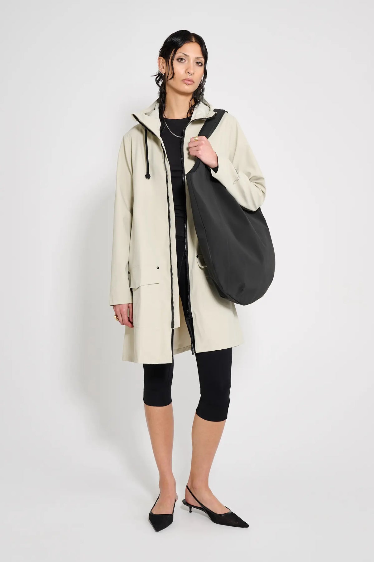 Model wearing Mosebacke Patch Pelican Raincoat in beige with a black bag, showcasing its stylish design and functionality.