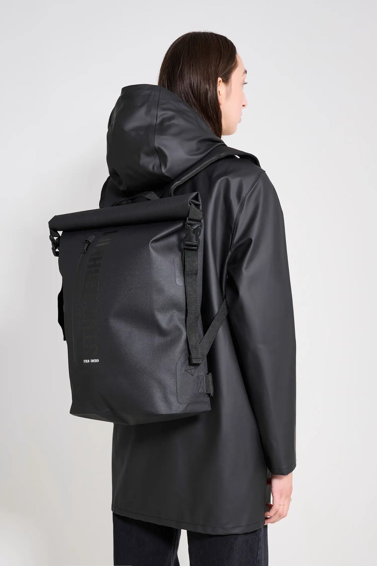 Model wearing Rain Rolltop 25L Black Backpack, showcasing its waterproof design and rolltop opening.