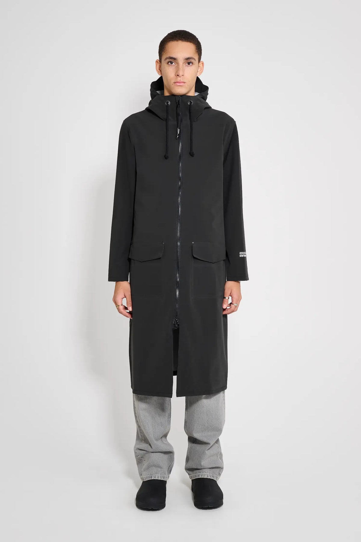 Stockholm Long Patch Black Raincoat modeled by a person, showcasing its oversized fit and waterproof design.