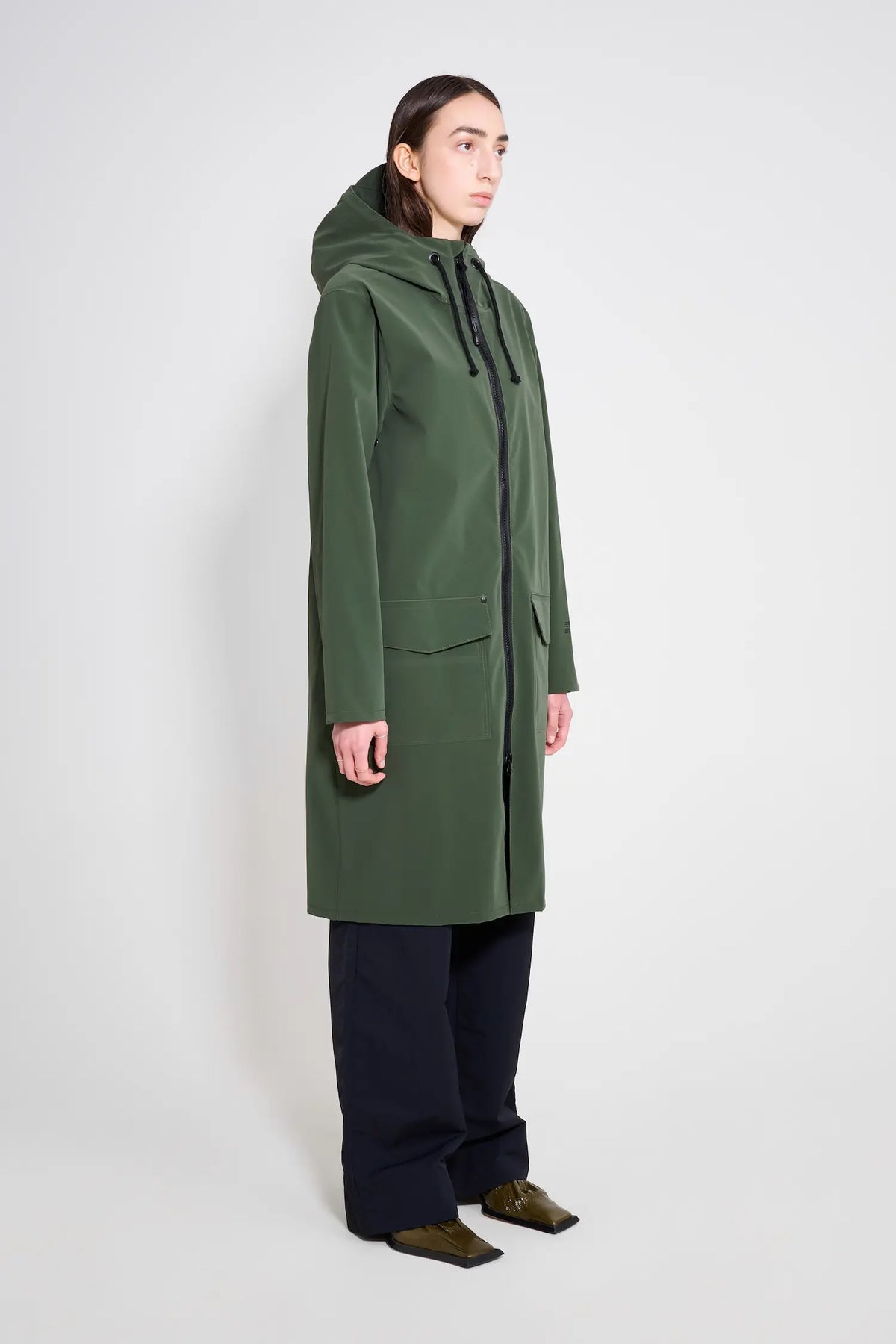 Stockholm Long Patch Matte Green Raincoat shown on model, featuring adjustable hood and patch pockets.