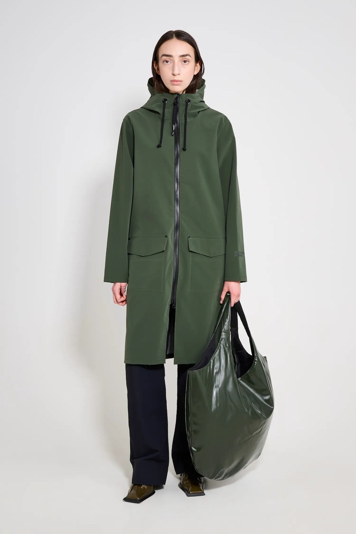 Model wearing Stockholm Long Patch Matte Green Raincoat with a black bag, showcasing a stylish and functional raincoat design.