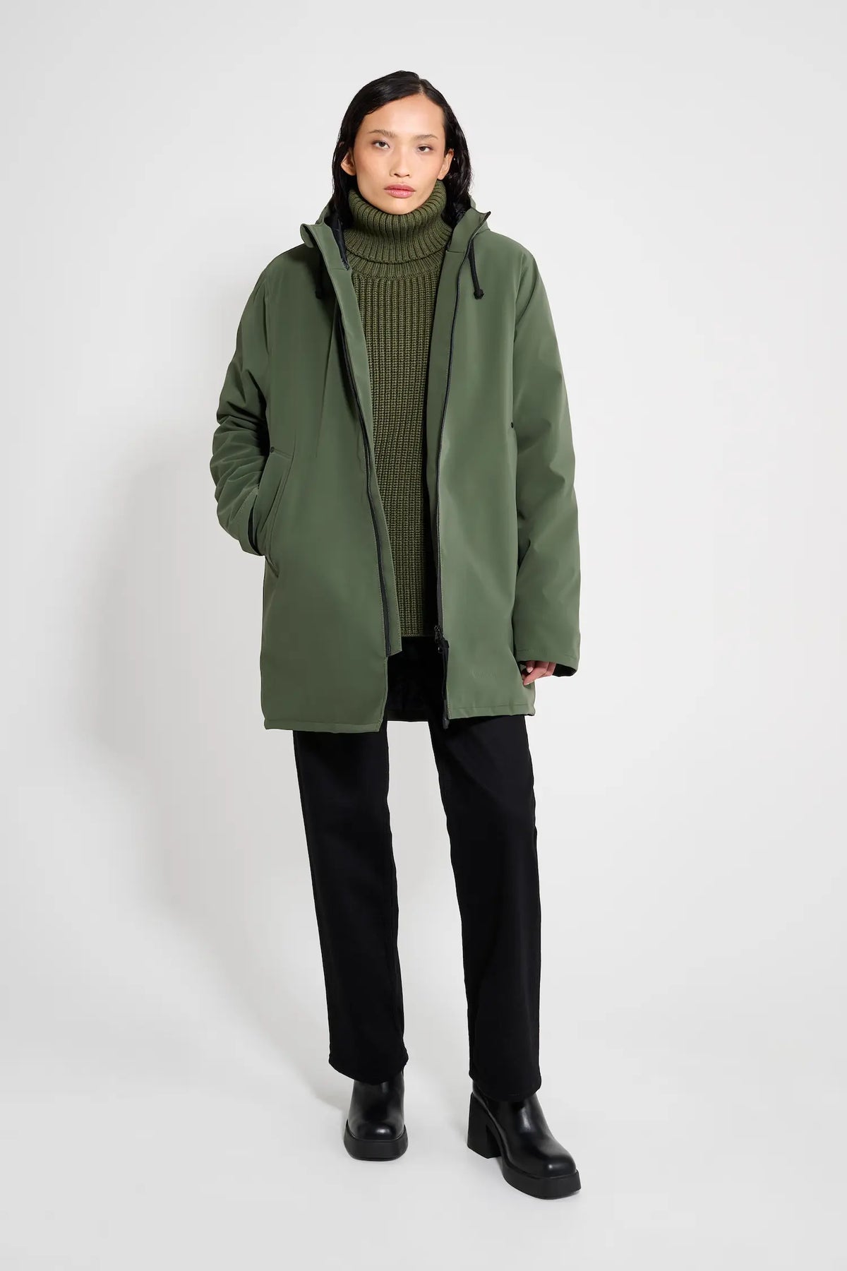 Model wearing a Stockholm Matte Green Winter Coat with a knitted turtleneck and black pants.