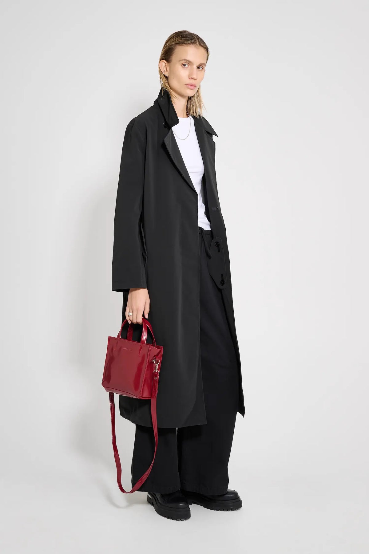 Model wearing Wayfair Black Trench Coat, stylish look with red handbag and casual outfit.