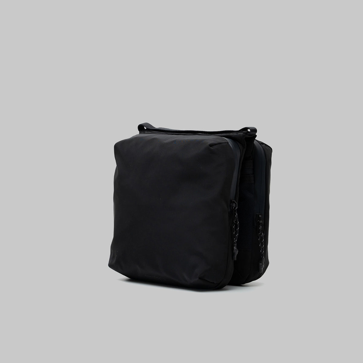Cassette Sacoche Medium Black Tech Sateen Bag from the side view, showcasing sleek design and zippered compartments.