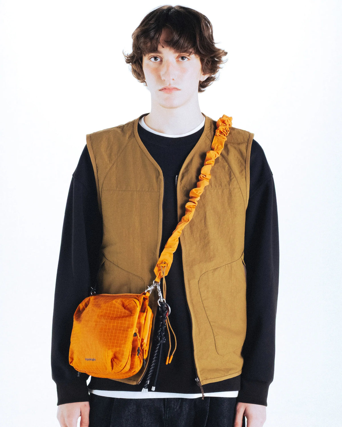 Man modeling the Cassette Sacoche Medium Black Tech Sateen Bag with an orange strap.