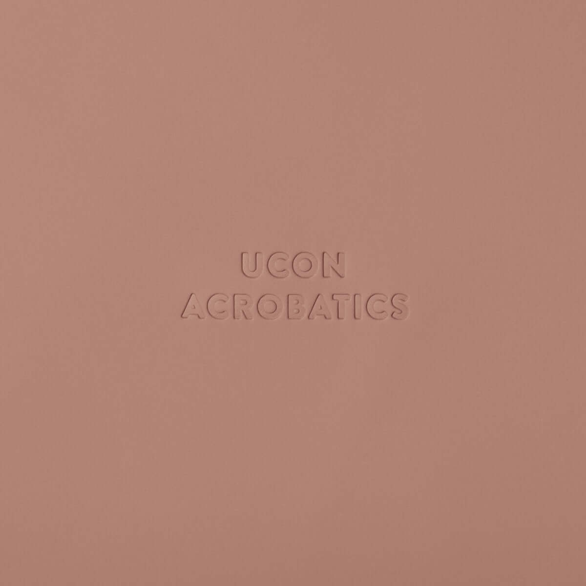 Ucon Acrobatics logo in embossed design on a soft pink background.