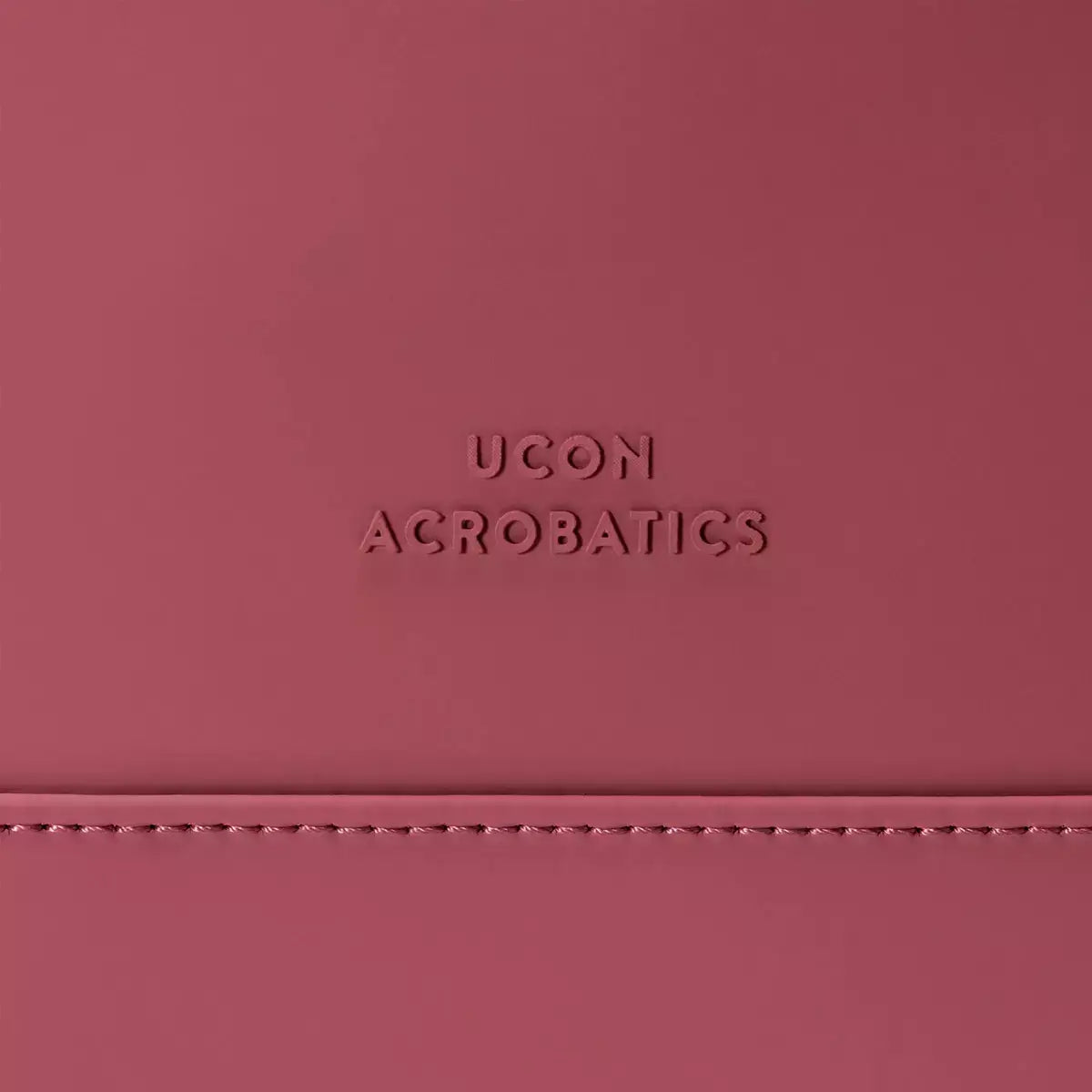 Close-up of UCON ACROBATICS logo embossed on pink material, showcasing sleek design and branding.