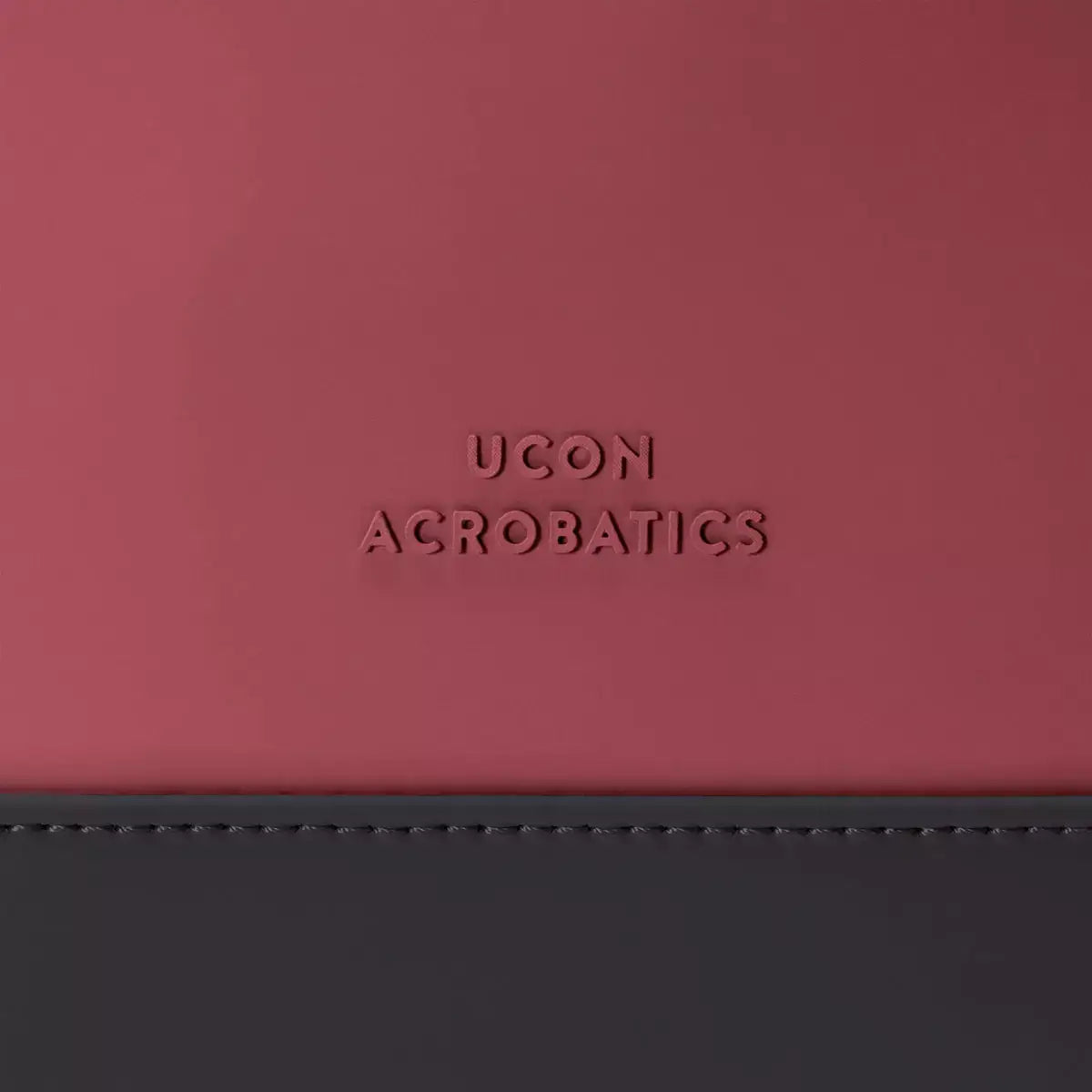 Logo detail of UCON ACROBATICS on a maroon and black bag's exterior.