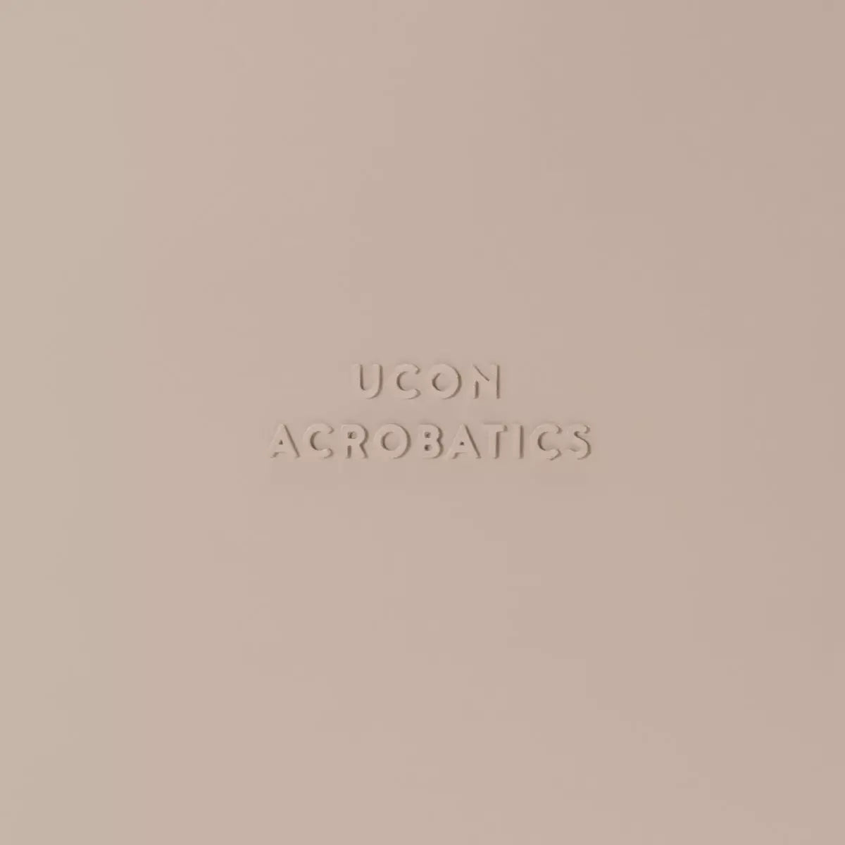Close-up of Ucon Acrobatics logo embossed in soft beige background.