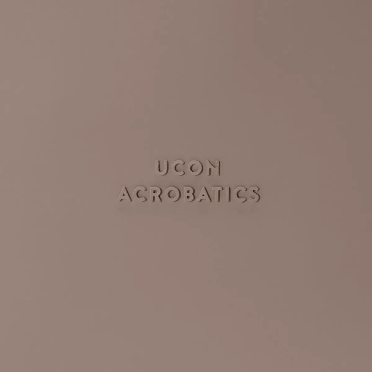 Close-up of the UCON ACROBATICS logo on a soft pink background.