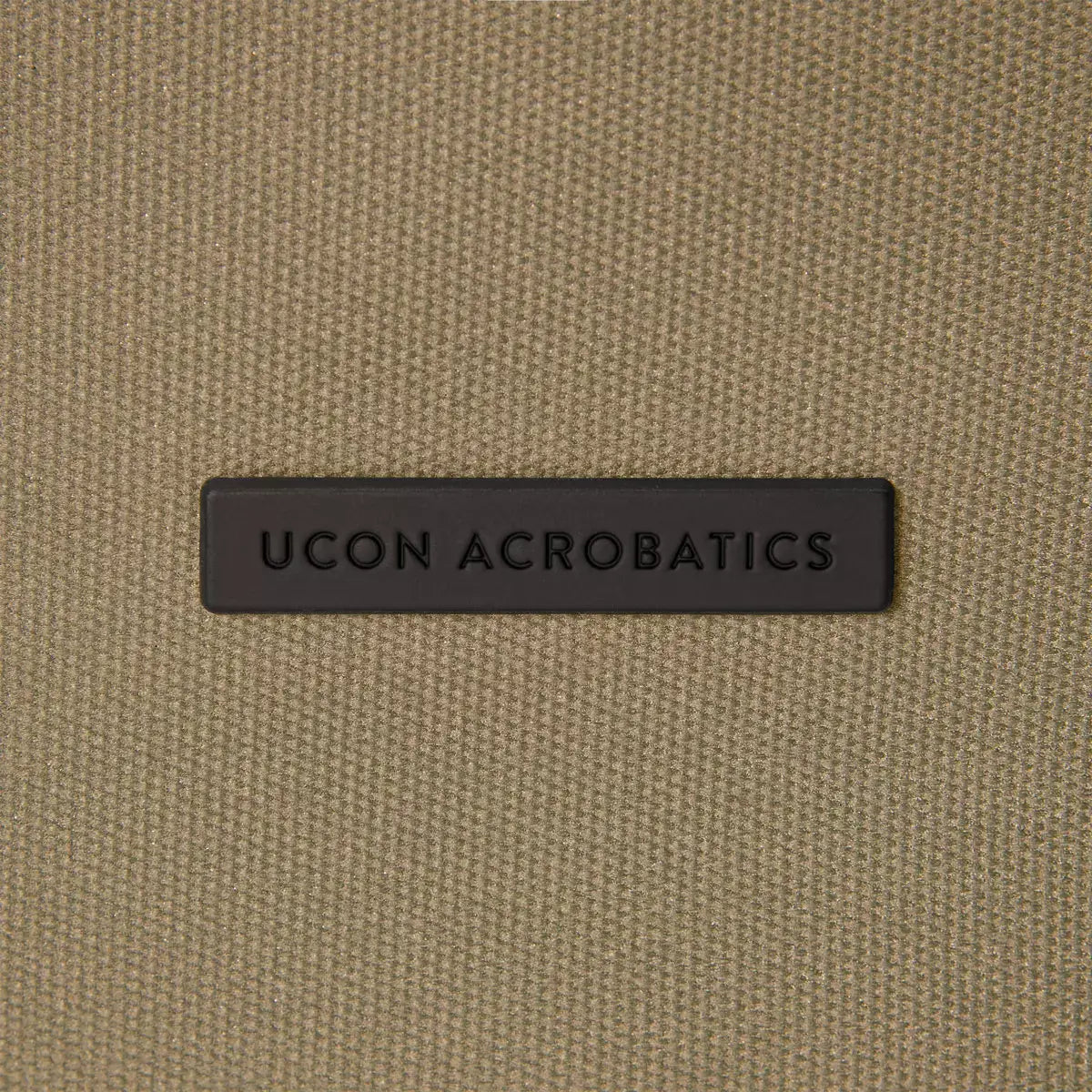 UCON ACROBATICS logo on a textured fabric background, showcasing brand details for Jannik Mini Phantom Olive Reflective Backpack.