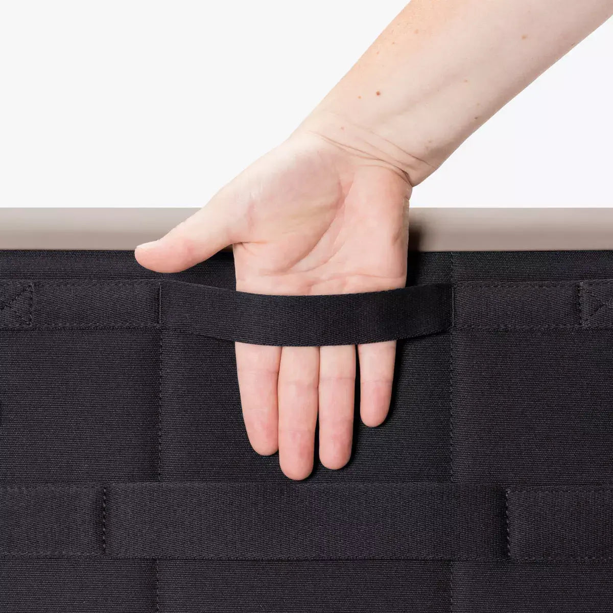 Hand holding a strap on a black storage bag featuring a durable design and easy carrying.