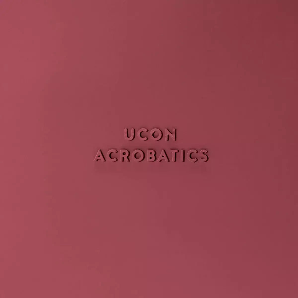 Ucon Acrobatics logo embossed on a burgundy background, showcasing stylish and modern branding.