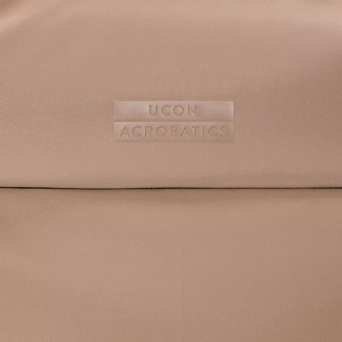 Close-up of UCON ACROBATICS logo on a beige fabric background.