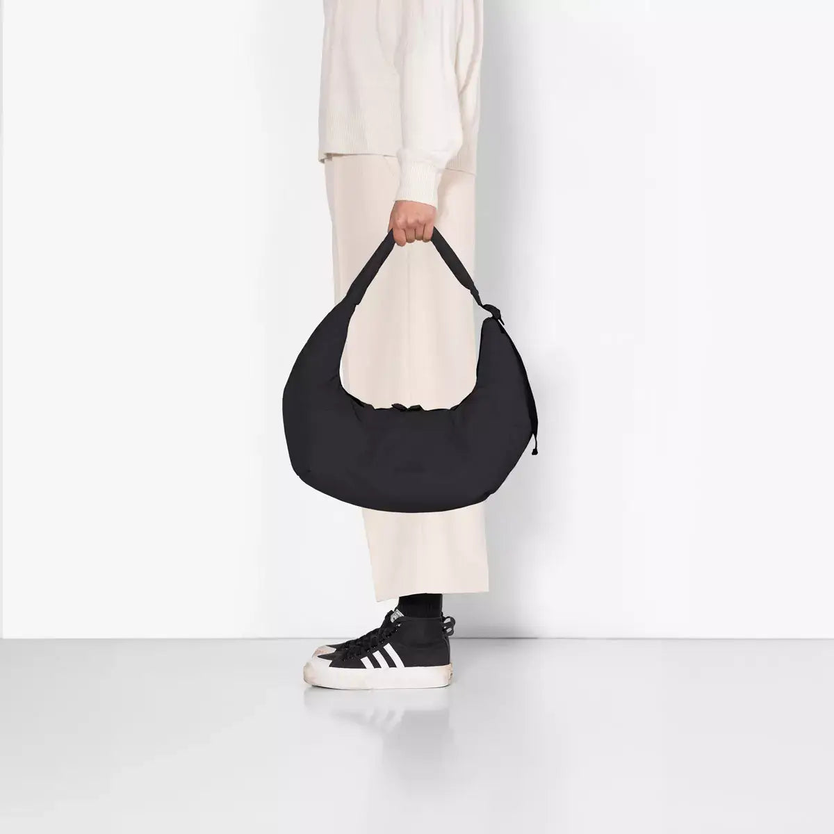 Shota Medium Moss Black Shoulder Bag held by a person in casual attire, showcasing its stylish design.