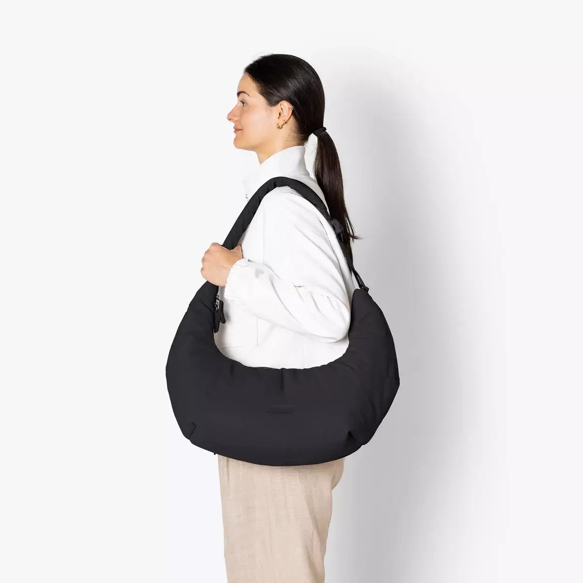 Shota Medium Moss Black Shoulder Bag being worn by a woman, showcasing its stylish design and padded adjustable strap.