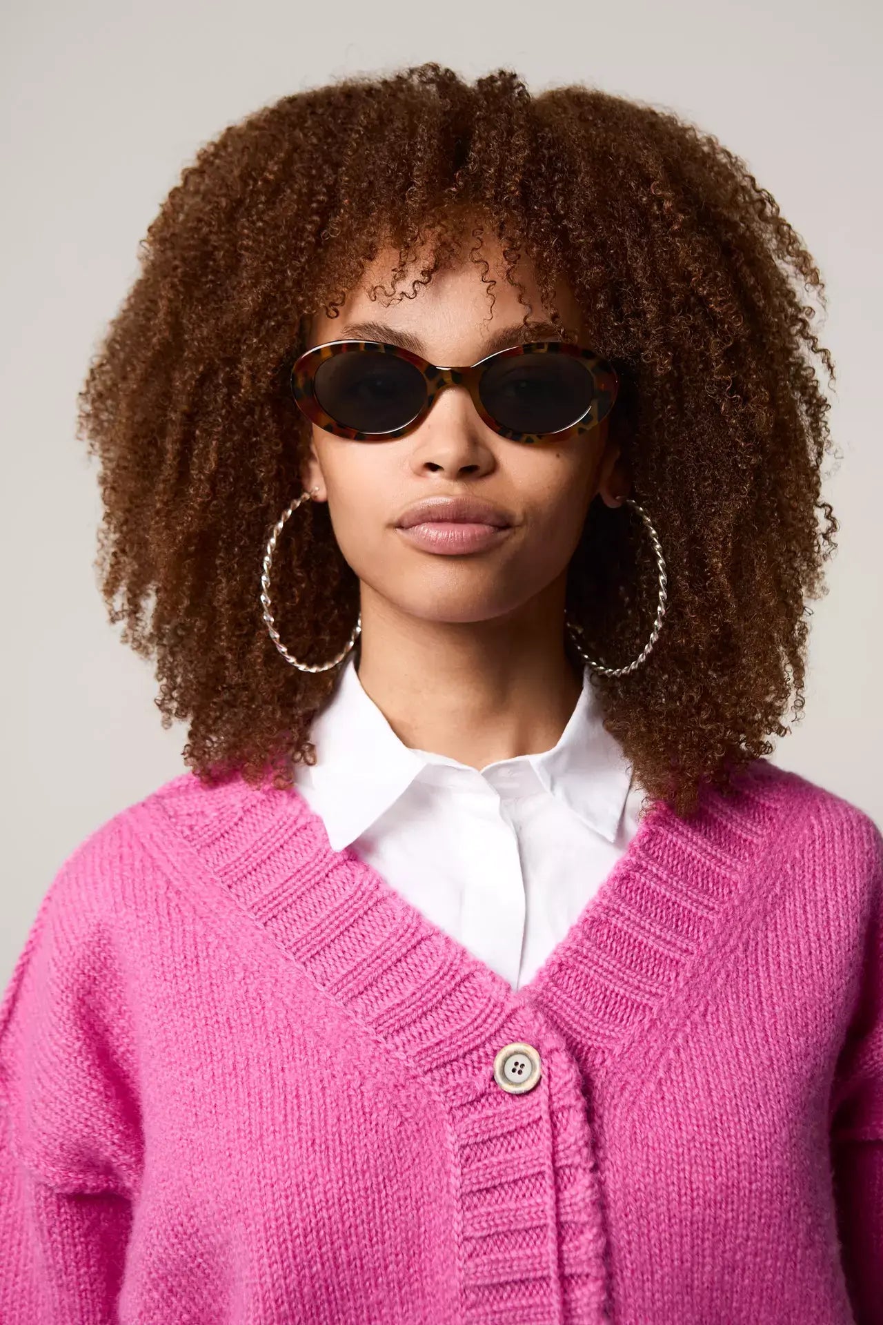 Model wearing Ana Amber Shell Sunglasses with a pink sweater and hoop earrings, showcasing UV 400 protection and eco-friendly design.