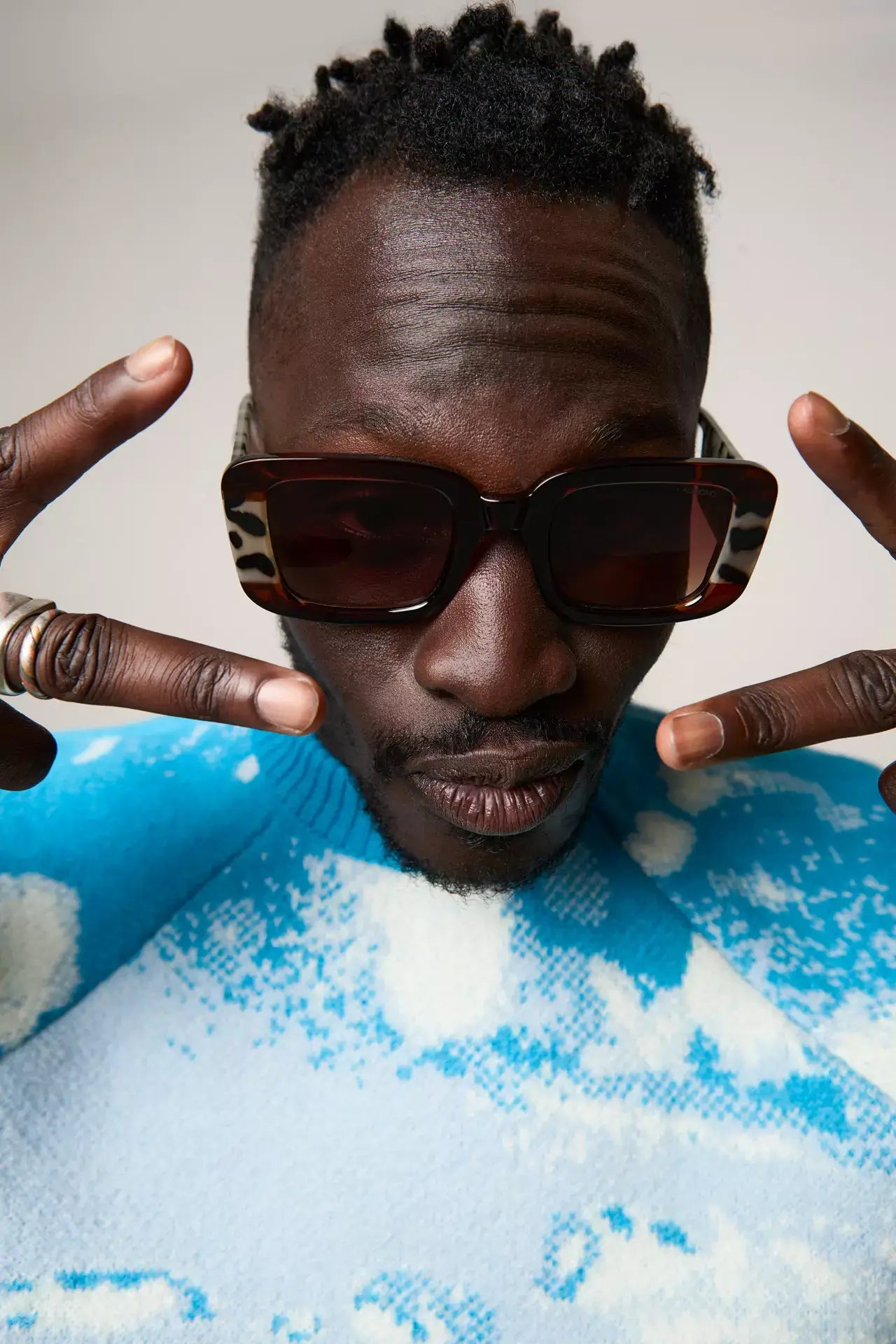 Avery Bronze Bobcoat Sunglasses worn by a man making peace signs in a colorful sweater.