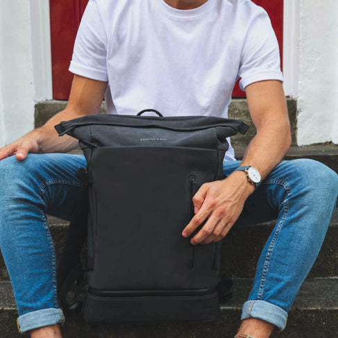 Helsinki Pro Sandstone Backpack displayed on a person sitting, showcasing its stylish design and functionality.