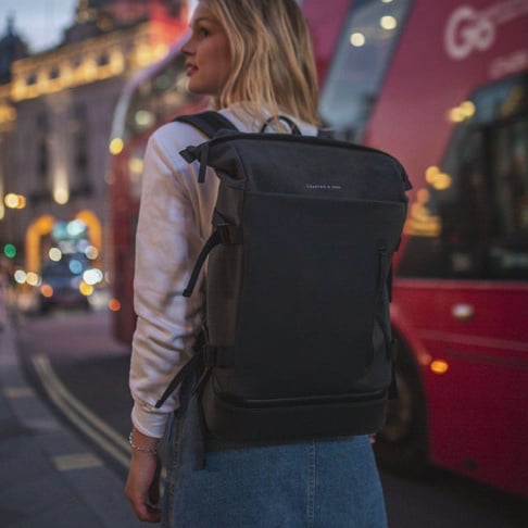 Helsinki Pro Sandstone Backpack being worn by a woman on a city street with a red double-decker bus in the background.