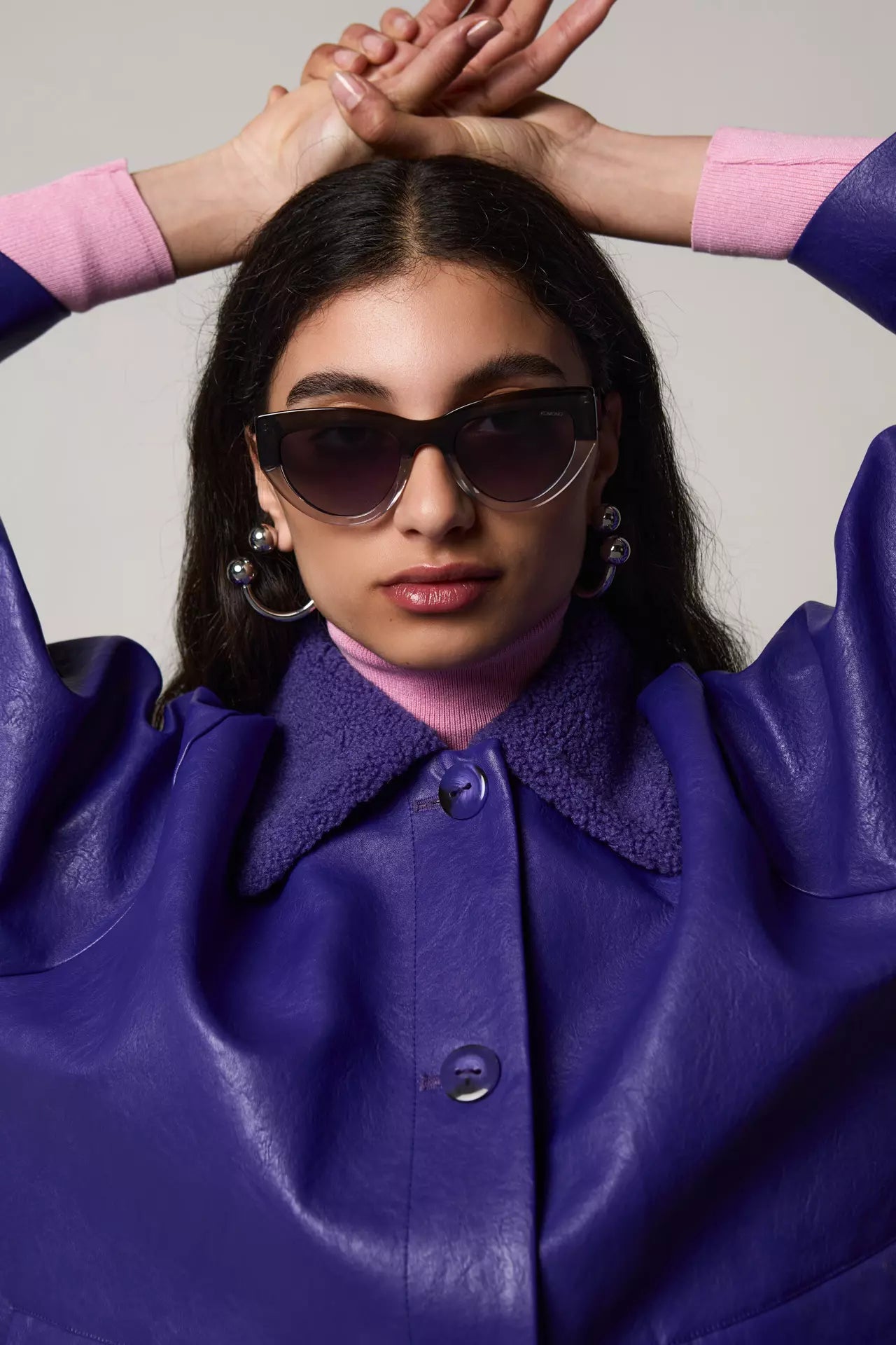 Woman wearing Kim Emerald Shadow Sunglasses with purple leather jacket and pink sweater, showcasing stylish eyewear.
