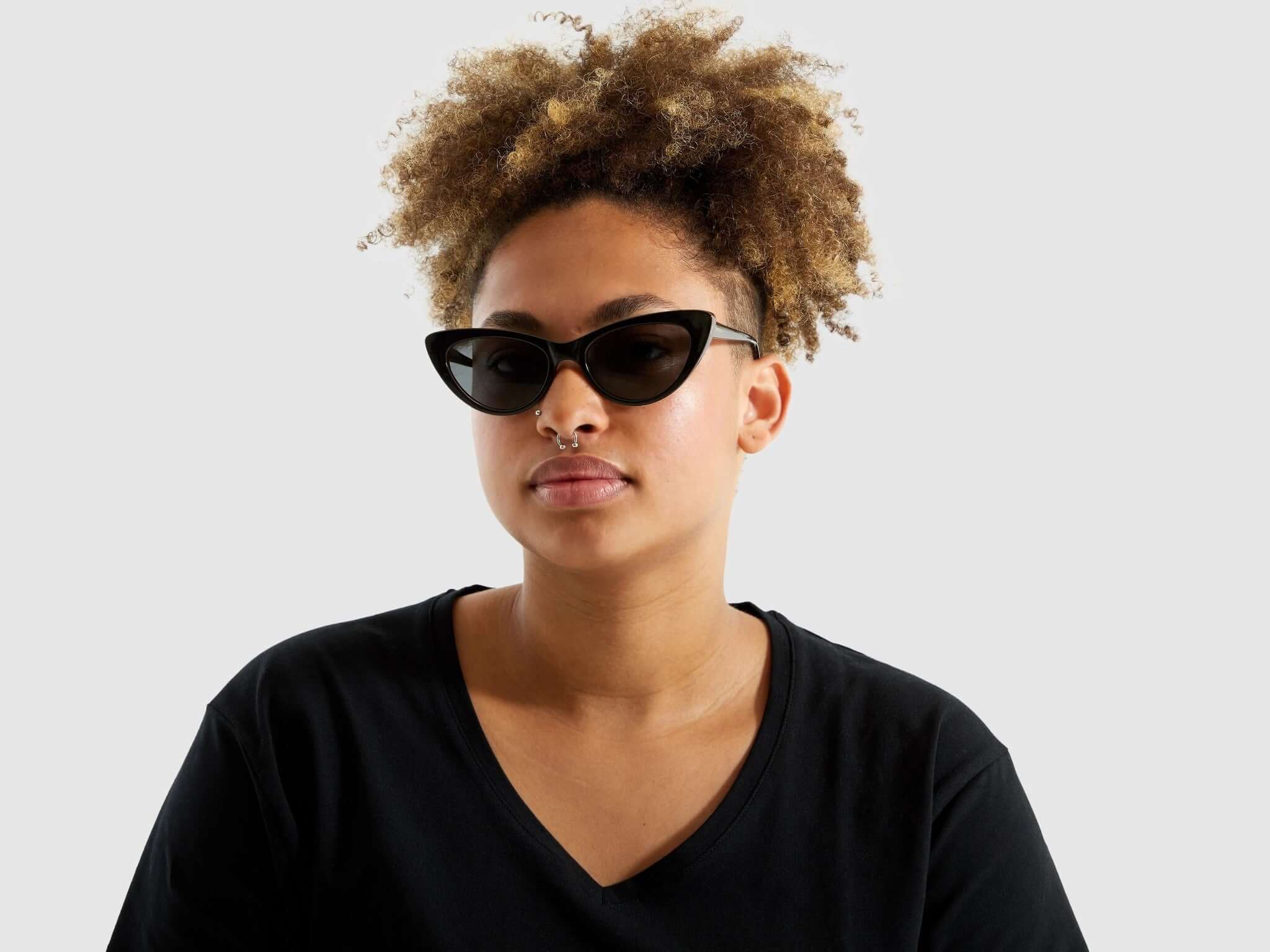 Model wearing Rosie Black Tortoise Sunglasses with black outfit and curly hair, showcasing stylish eyewear.