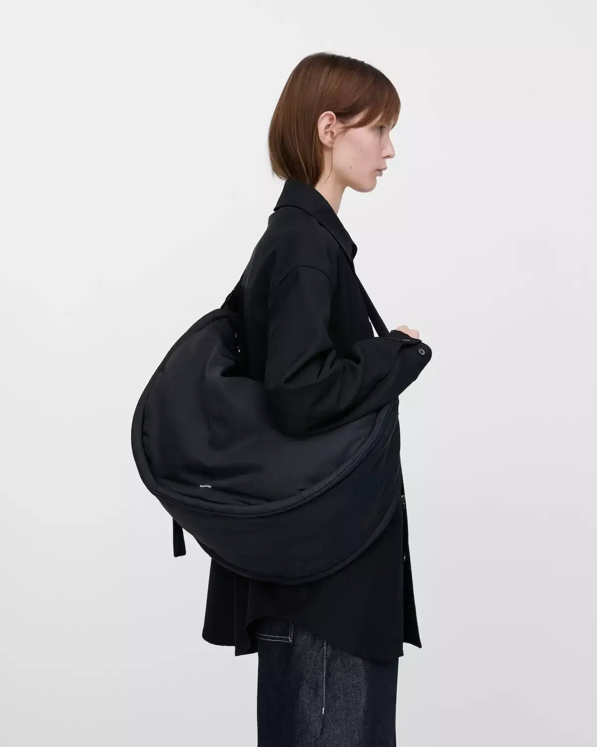 Model showcasing the Curve Crossbody Round L Black Shoulder Bag, highlighting its round shape and sleek design.