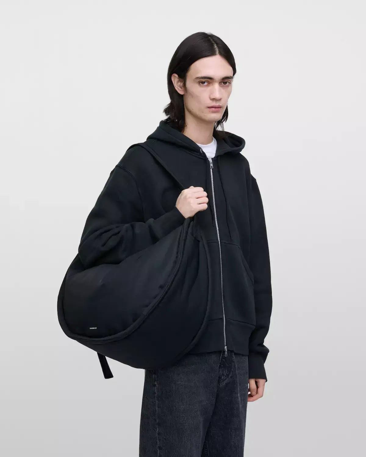 Model carrying Curve Crossbody Round L Black Shoulder Bag in a casual outfit with a hoodie.