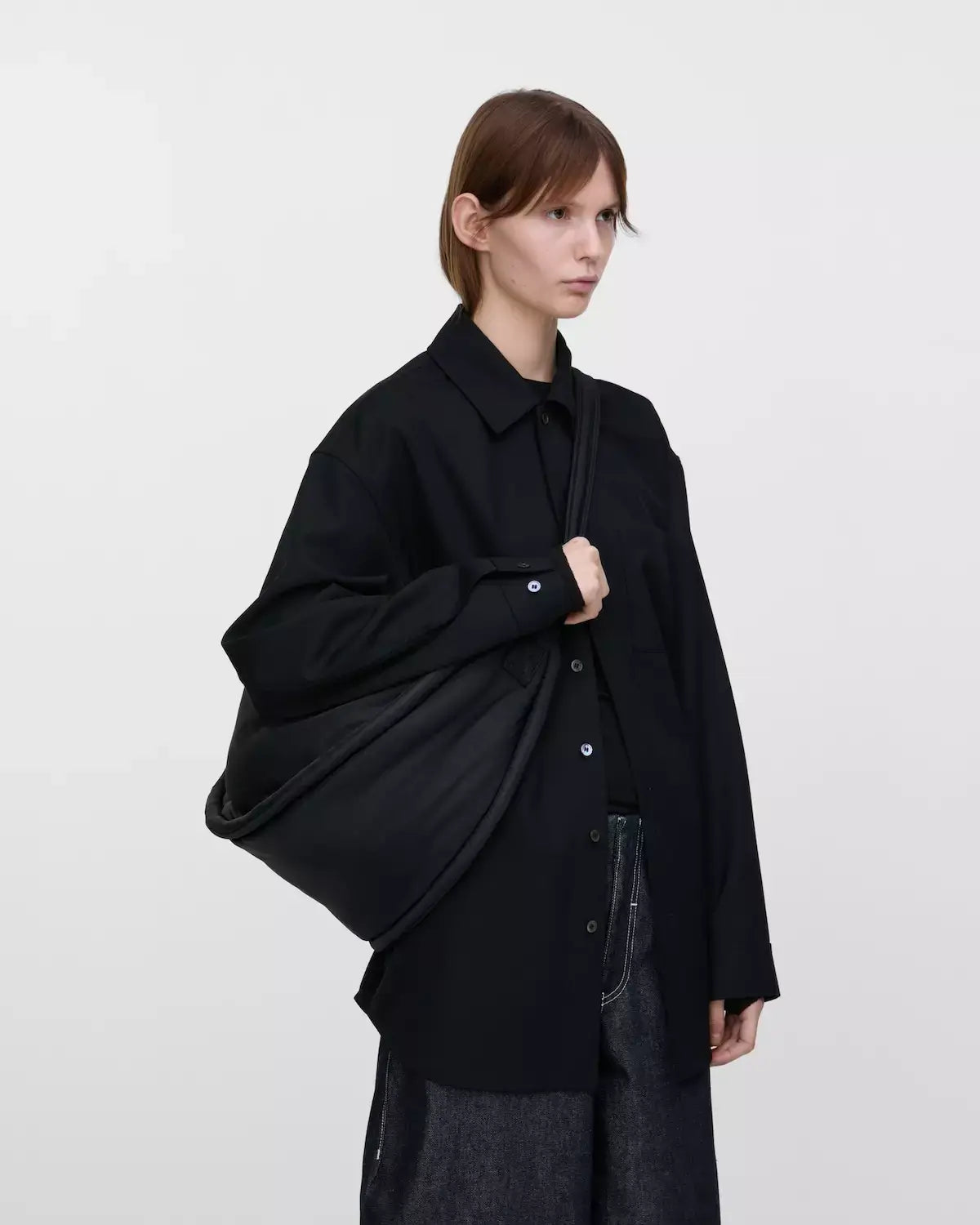 Model showcasing the Curve Crossbody Round L Black Shoulder Bag on a black shirt outfit.