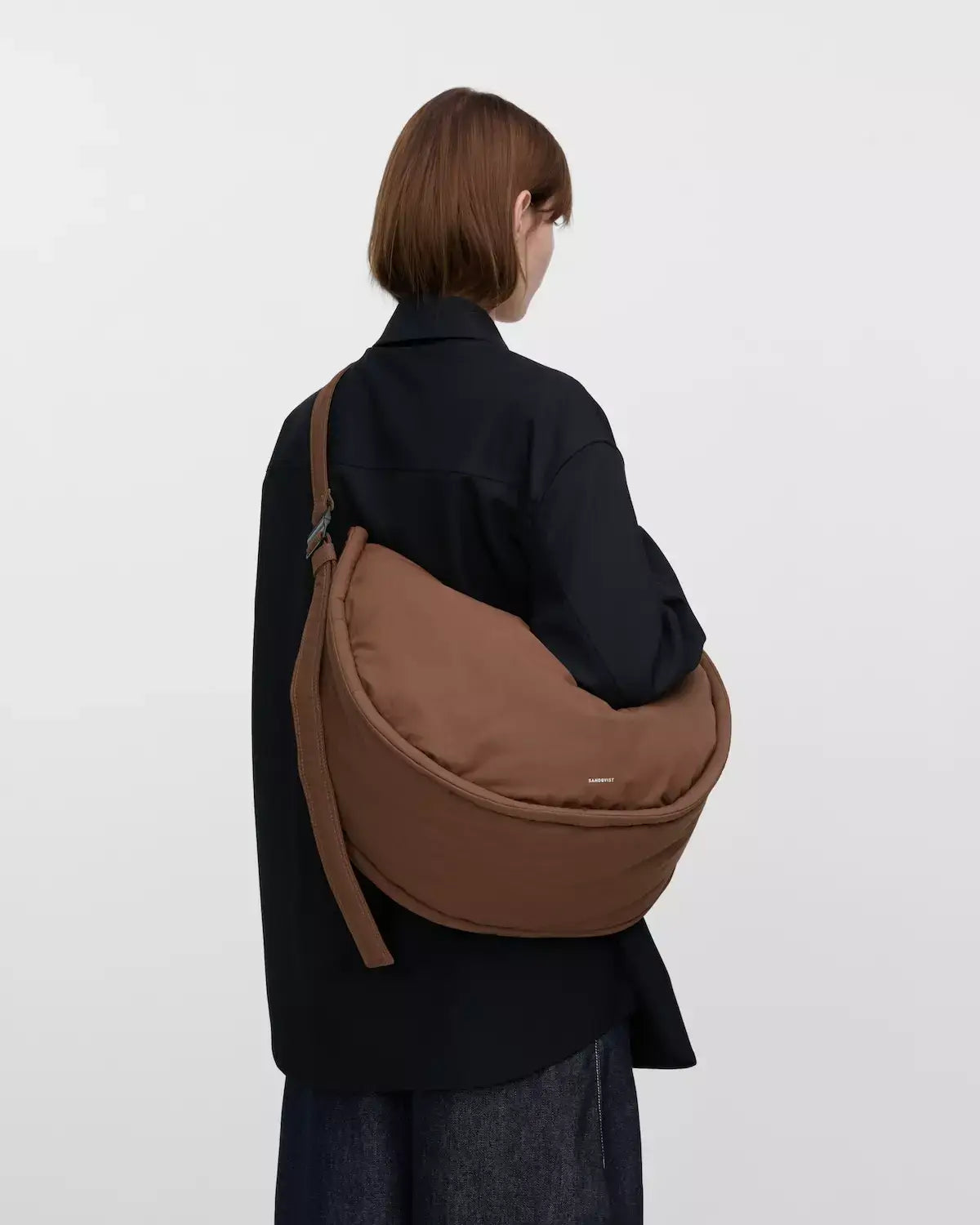 Woman wearing Curve Crossbody Round L Dark Taupe Shoulder Bag in a stylish outfit.