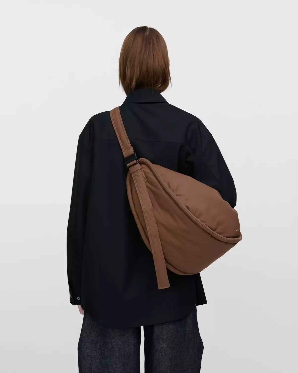 Model wearing the Curve Crossbody Round L Dark Taupe Shoulder Bag, showcasing its stylish design and padded strap.