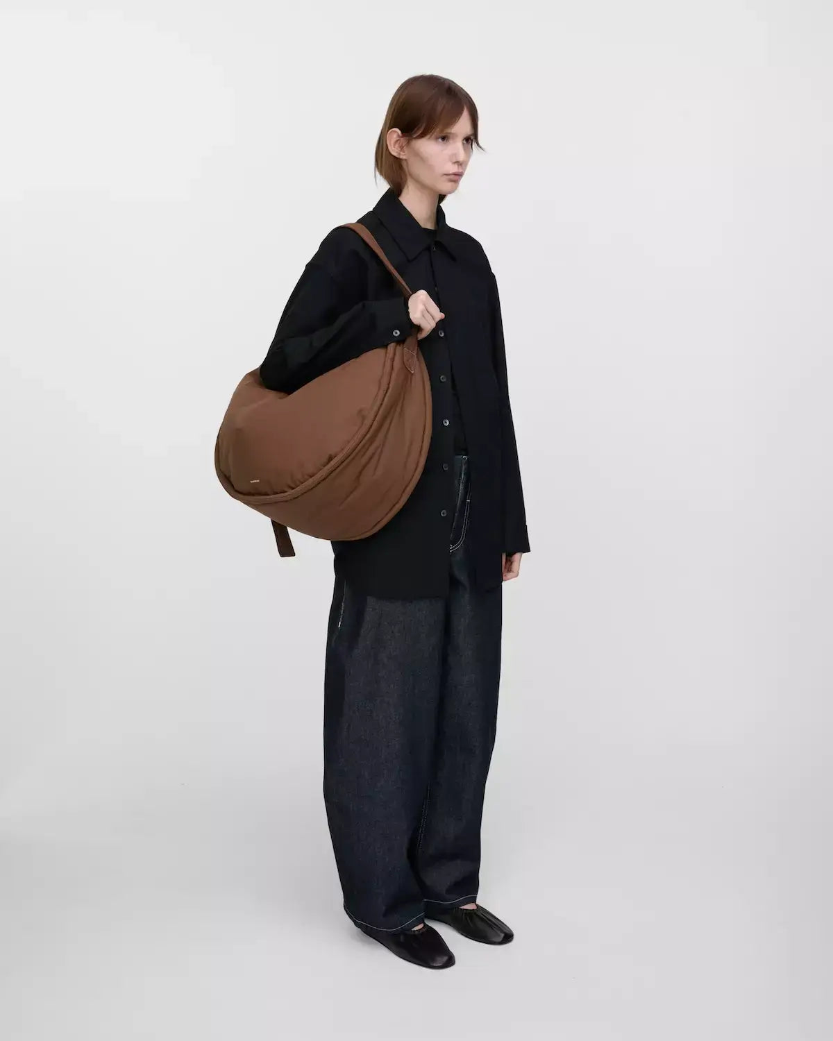 Model holding Curve Crossbody Round L Dark Taupe Shoulder Bag, showcasing its stylish design and functionality.
