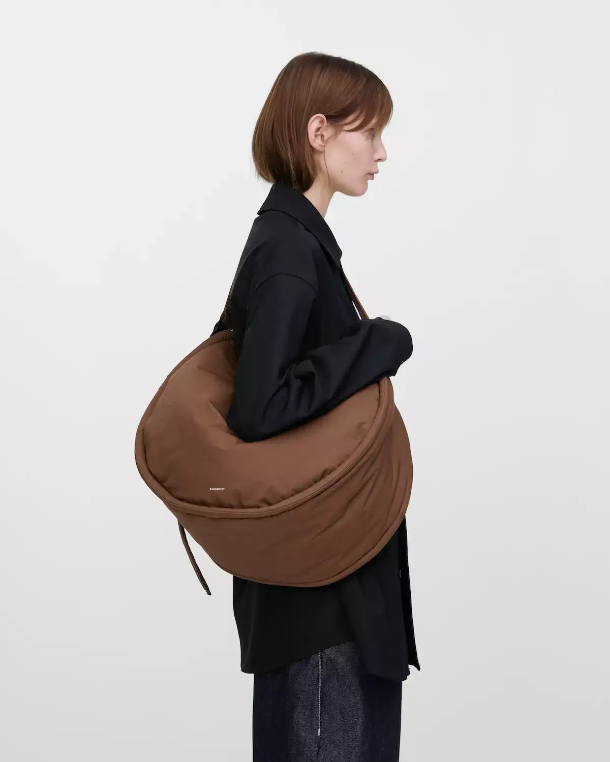Curve Crossbody Round L Dark Taupe Shoulder Bag shown in profile, showcasing its water-resistant design and padded strap.