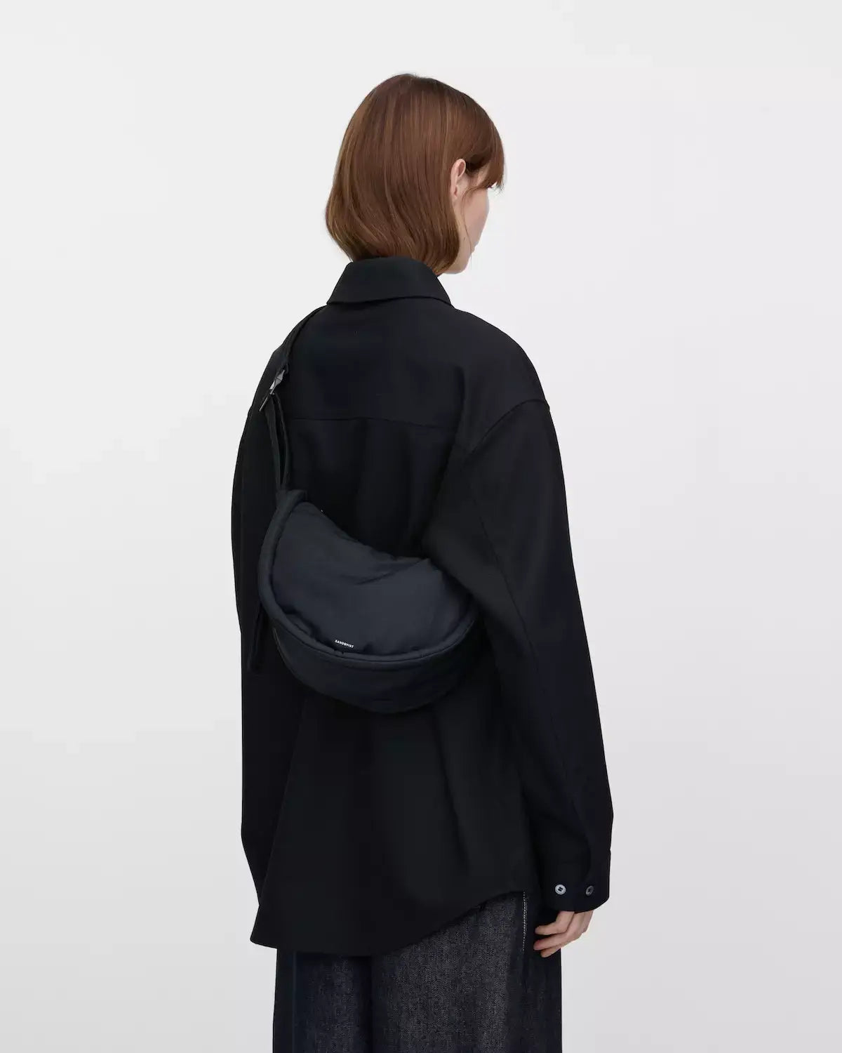 Woman wearing a Curve Crossbody Round S Black Shoulder Bag in black attire, showcasing stylish crossbody design.