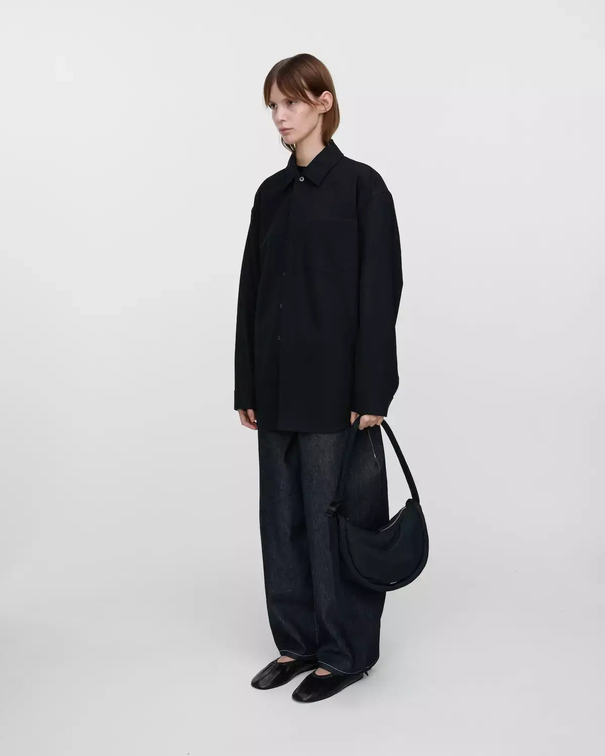 Woman in black shirt holding Curve Crossbody Round S Black Shoulder Bag, showcasing its stylish design.
