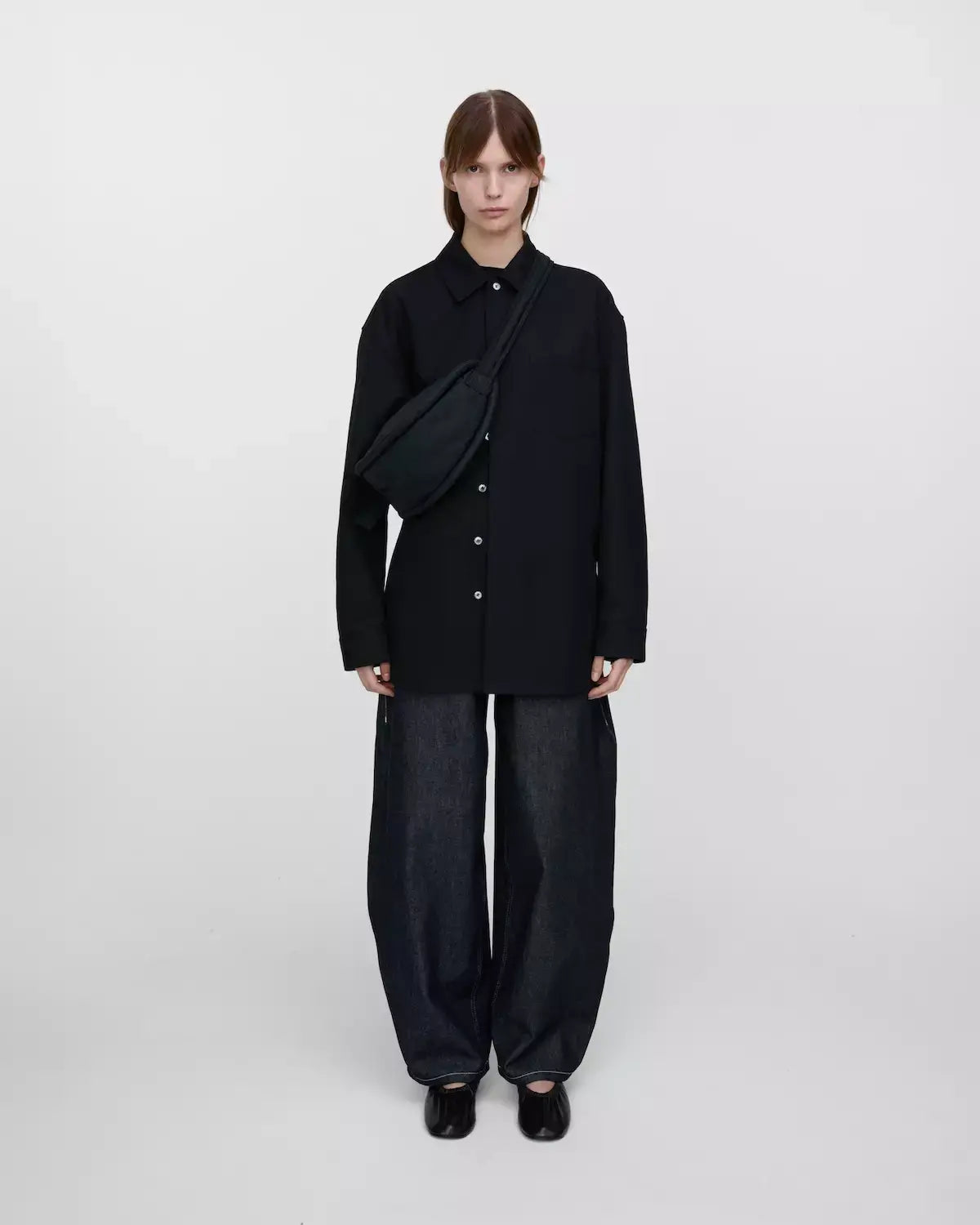 Model wearing Curve Crossbody Round S Black Shoulder Bag with oversized black shirt and dark jeans.